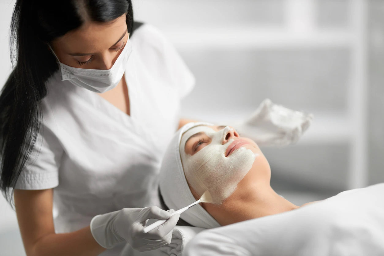 Woman receiving a facial mask treatment from a professional in a clinical setting.